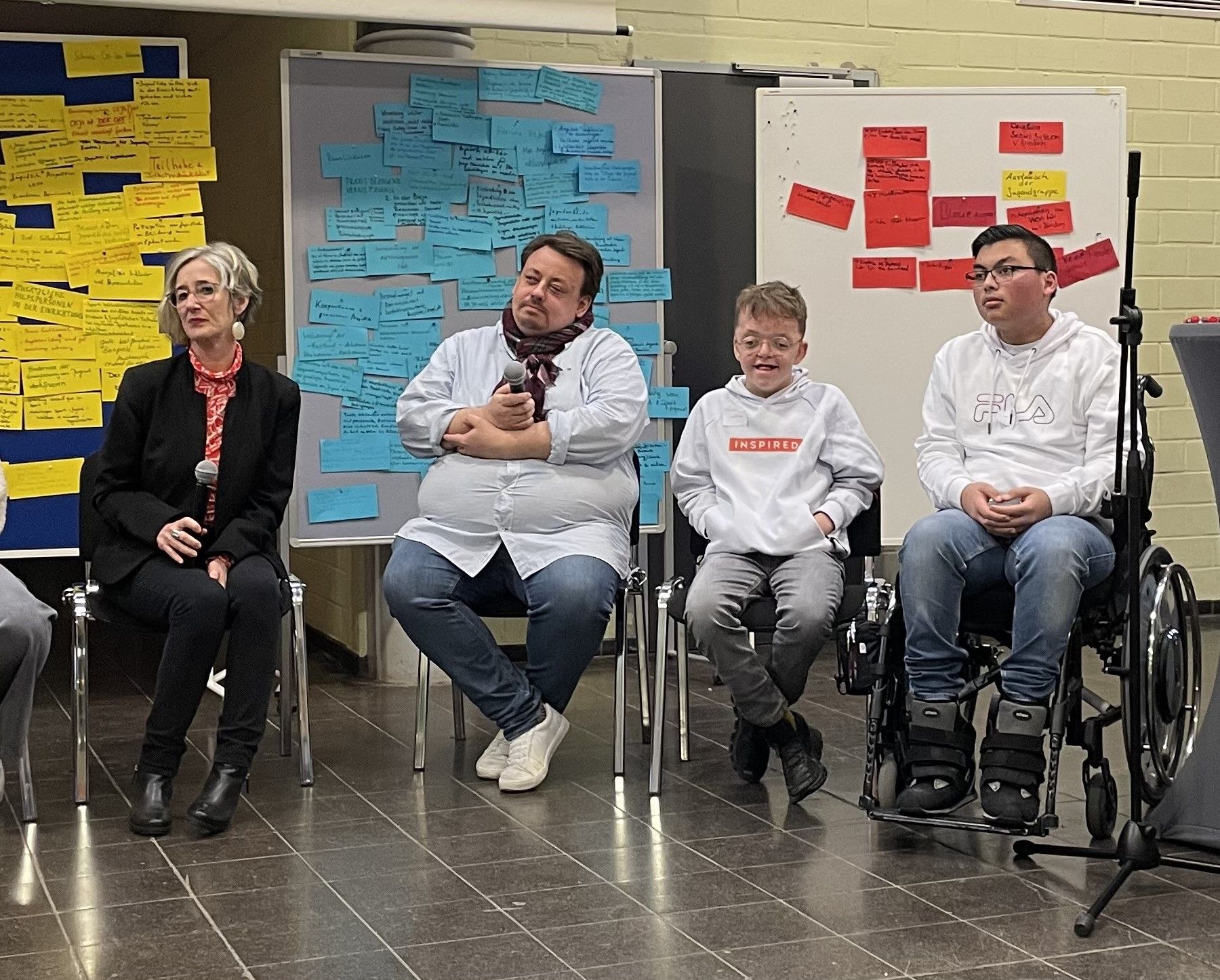 Eiine Frau, ein Mann und zwei Schüler setzten nebeneinander auf Stühlen.