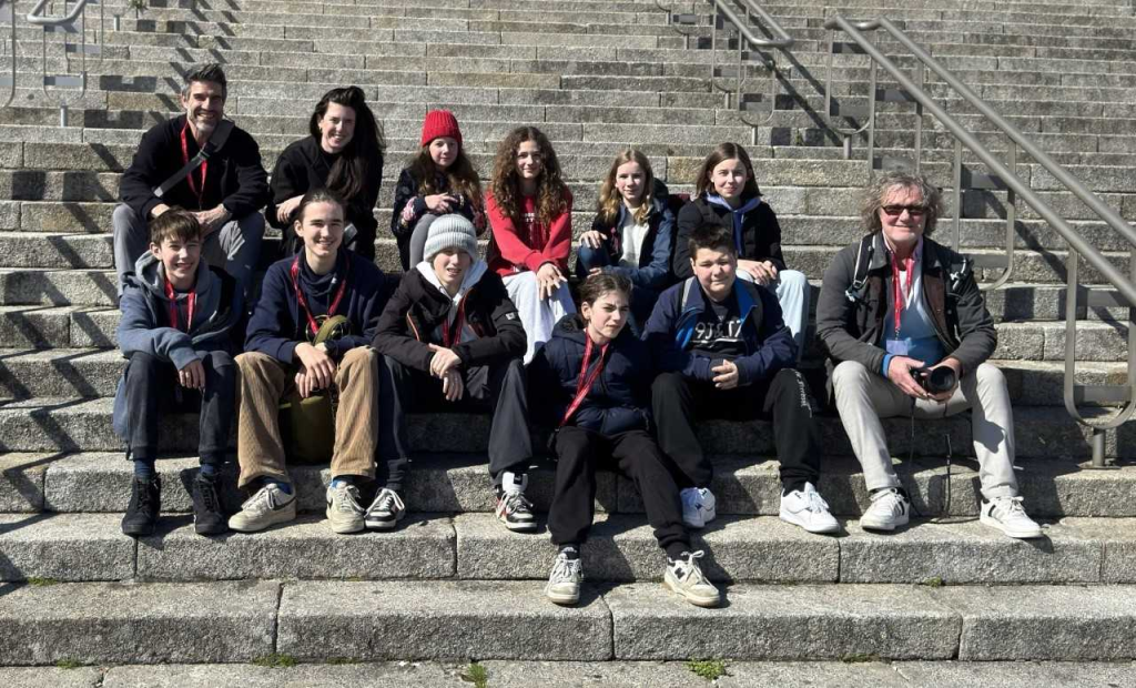 Eine Gruppe von mehreren Schüler*innen sitzen auf 3 Stufen verteilt auf einer Treppe.