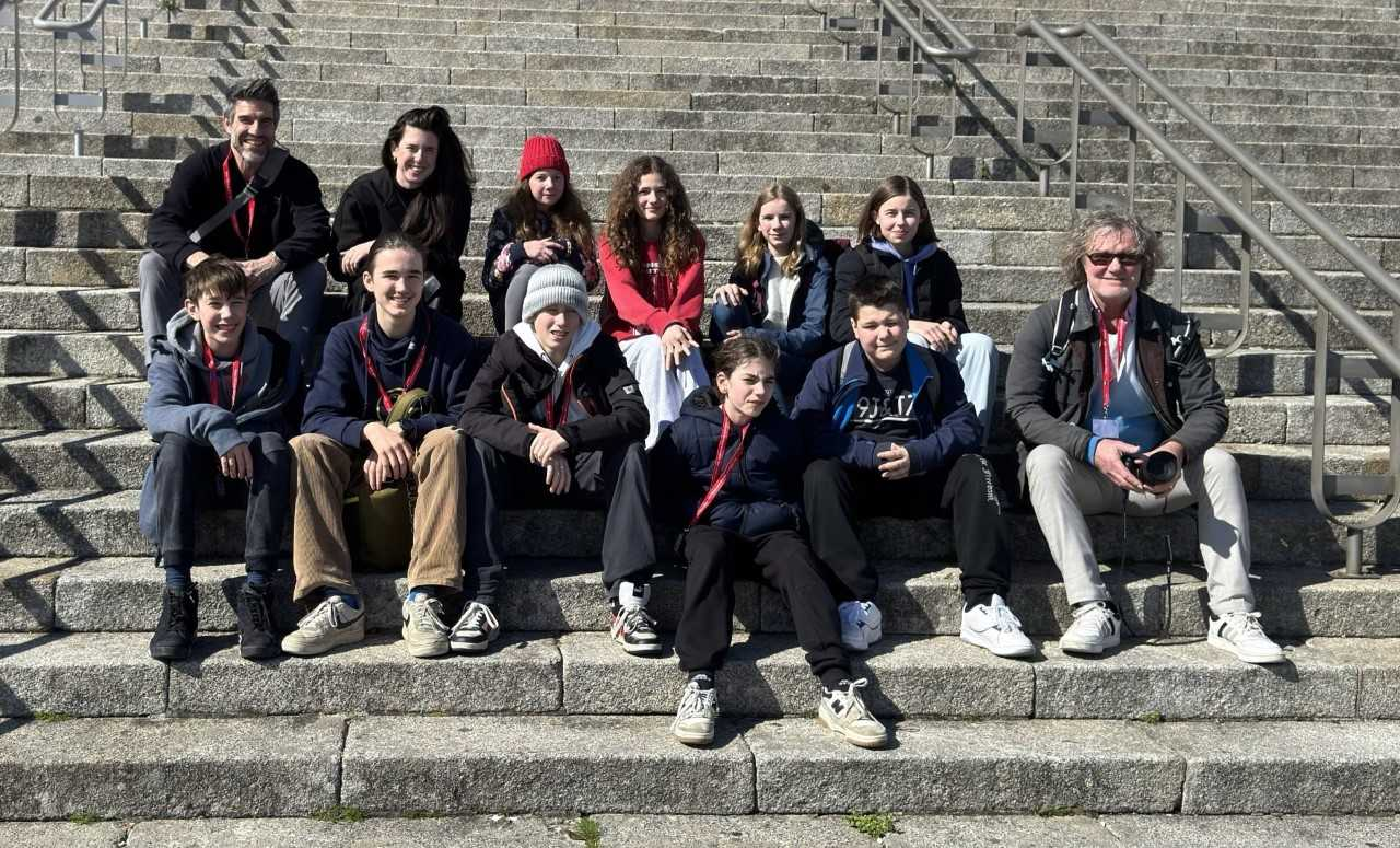 Eine Gruppe von mehreren Schüler*innen sitzen auf 3 Stufen verteilt auf einer Treppe.