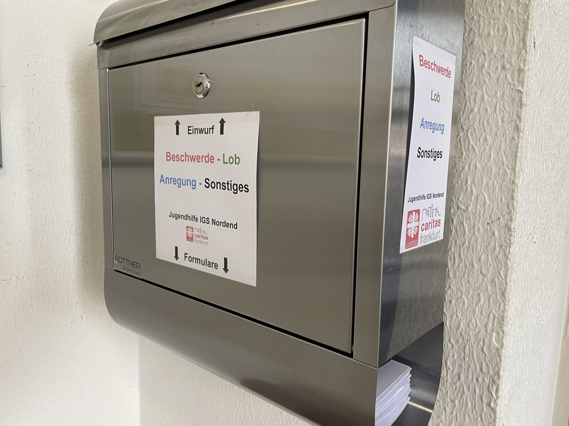 Ein Blick von der Seite auf einen Metallbriefkaasten. An der Seite und an der Vorderfront hängen Schilder mit der Aufschrift: Beschwerde, Lob, Anregung, Sonstiges