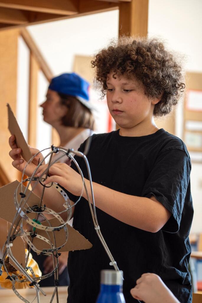Ein Schüler mit Locken biegt Draht, der aussieht wie das Skelet eines Dinosauriers