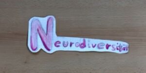 Das Wort "Neurodiversität" mit Buntstiften auf Papier geschrieben und ausgeschnitten liegt auf einem Holzplatte