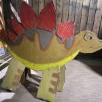 Ein Dinosaurier mit roten Stacheln auf dem Rücken und gelben Füßen aus Pappe angefertigt