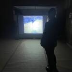 Eine Person steht vor einer großen hellen Projektion an einer Wand.