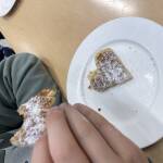Eine Herzchenwaffel auf dem Teller, eine angebissene Waffelteil in einer Hand.